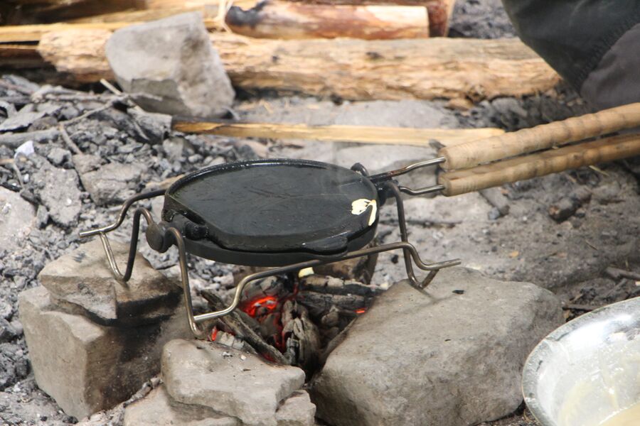 Eine gusseiserne Pfanne hängt über einem Lagerfeuer zwischen Feldsteinen.