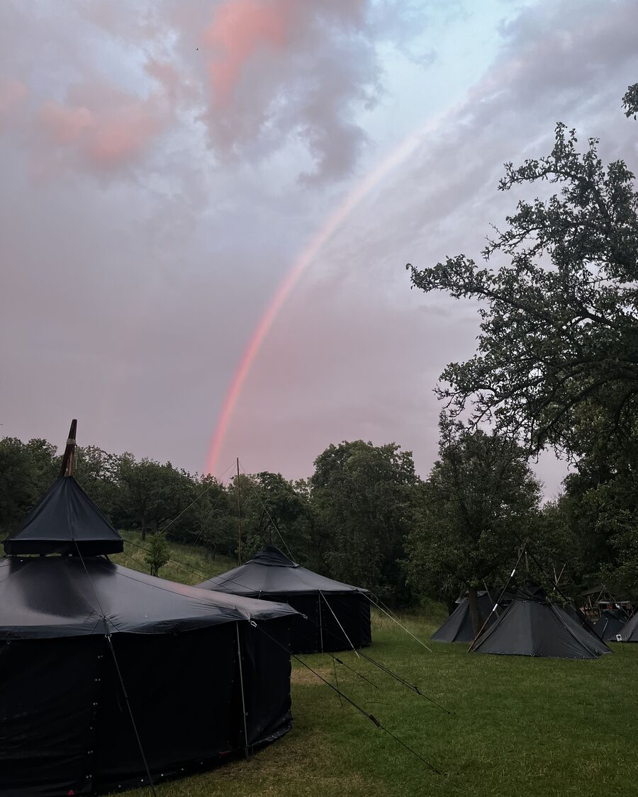 Ein Regenbogen steht über einem Zeltlager mit Jurten und Kohten am Abend.